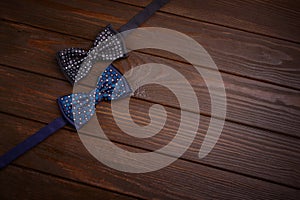 Two dark bowties with polka dots on a dark brown wooden board background.