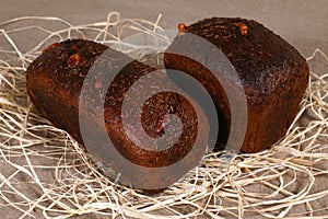 Two dark bread stuffed with cheese lying in straw on grey linen