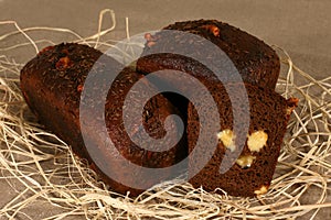 Two dark bread stuffed with cheese lying in straw on grey linen