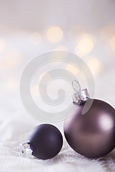 Two dark Christmas balls on white lace on light and warm bokeh b