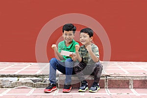 Two dark-haired Latino children who are brothers or friends who live in poverty play video games with a cell phone, make video cal