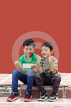 Two dark-haired Latino children who are brothers or friends who live in poverty play video games with a cell phone, make video cal