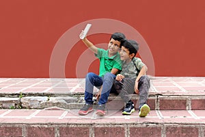 Two dark-haired Latino children who are brothers or friends who live in poverty play video games with a cell phone, make video cal