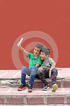 Two dark-haired Latino children who are brothers or friends who live in poverty play video games with a cell phone, make video cal