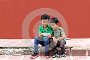 Two dark-haired Latino children who are brothers or friends who live in poverty play video games with a cell phone, make video cal