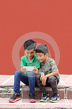 Two dark-haired Latino children who are brothers or friends who live in poverty play video games with a cell phone, make video cal