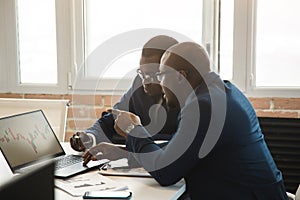 Two dark-skinned partners of an African American businessman in a meeting work on a laptop in the office. Affordable