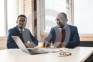 Two dark-skinned partners of an African American businessman in a meeting work on a laptop in the office. Affordable