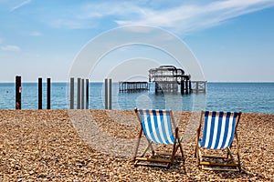 Two deck chairs on the pebble beach at Brighton on the Sussex coast, with the old West Pier behind