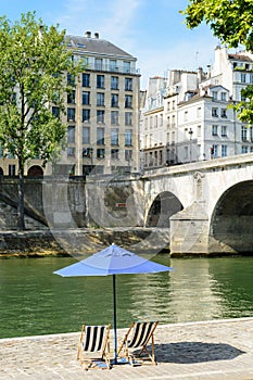 Two deck chairs in the sun under a parasol on the wharf of the river Seine