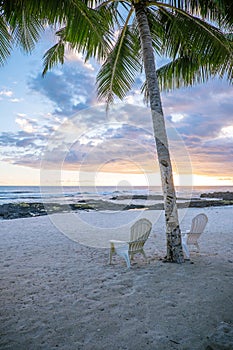 Two deck chairs under palm tree at sunset on an empty beach at L