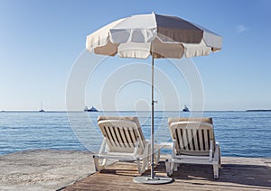 Two deckchairs under a parasol against the backdrop of a calm sea on a clear sunny day. Idyll and relaxation. Travel and tourism.