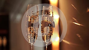 Two decorated wedding champagne glasses with bubbles stand on a table