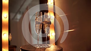 Two decorated wedding champagne glasses with bubbles stand on a table