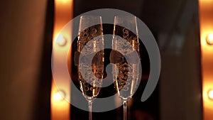 Two decorated wedding champagne glasses with bubbles stand on a table