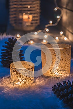 Two decorative glasses with tealights on a lambskin on a veranda in the blue hour, fairy lights and candle light in the background