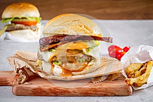 Two delicious burgers with cheddar cheese, bacon and oozing sauce over wooden board and wooden background