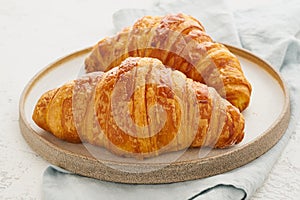 Two delicious croissants on plate and hot drink in mug. Morning French breakfast with fresh pastries. Light gray background