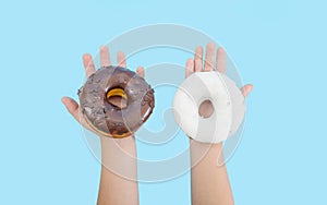 Two delicious donuts with black and white chocolate icing in children`s hands isolated on a blue background. Donuts in children`s