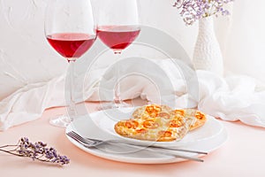 Two delicious heart-shaped pizzas on plates and two glasses of wine on a set table to celebrate valentine's day