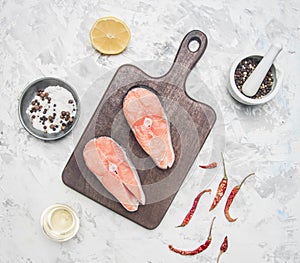 Two delicious raw salmon steaks with lemon, seasoning pepper on a white background, top view