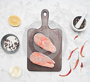 Two delicious raw salmon steaks with lemon, seasoning pepper on a white background, top view