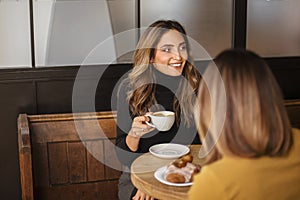 Two delighted women girlfriends drinking coffee and talking during meeting in cozy cafe