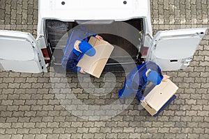 Two Delivery Men Unloading Cardboard Box From Truck