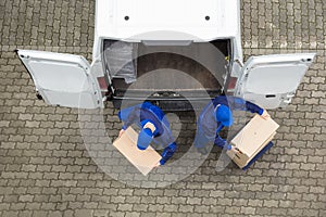 Two Delivery Men Unloading Cardboard Box From Truck