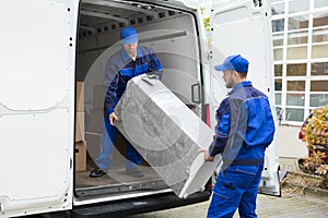 Two Delivery Men Unloading Furniture From Vehicle