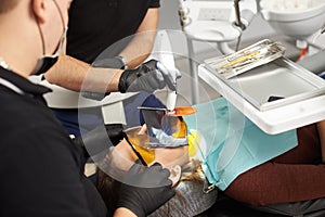 Two dentists in black suits fixing the teeth of a patient with a kofferdam on the face