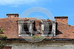 Two destroyed roof windows with rusted metal flower holders on abandoned old building with broken and missing roof tiles
