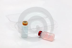 Two different colors vaccine bottle inside and one outside an opened translucent plastic box for ten vaccine bottles
