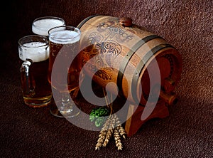 Two different glasses with light beer, a wooden keg, hops and ears of corn on a brown background