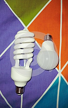 two different shape of light bulb : spiral bulb and globe bulb laying opposite on fabric