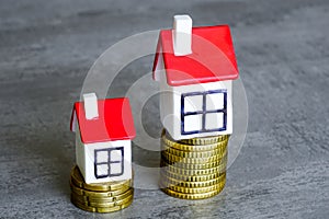 Two different sizes tiny houses on two different height stacks of coins symbolizing different costs