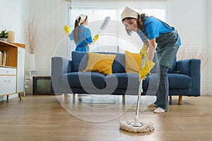 Two diligent Asian maids collaborate seamlessly, cleaning the living room with precision and efficiency, leaving no corner