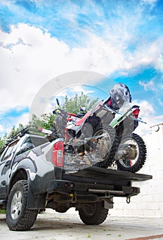 Two dirt bike motorcycles on the back of the camo truck with safety gear.