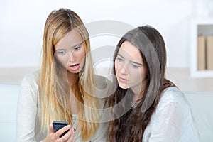 Two displeased young women looking at mobile phone