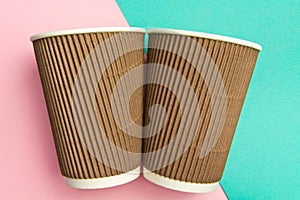 Two disposable cups for hot drinks on a geometric pink and turquoise backgrounds. Paper cups