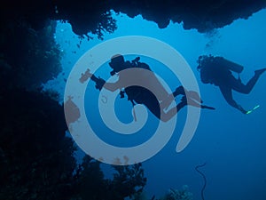 Two divers are silhouetted through cave and coral