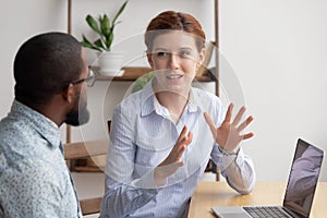 Two diverse businesspeople chatting sitting behind laptop in office