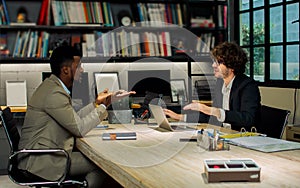 Two diverse Caucasian and African businessman seriously discussing with argument, disputing while sitting in modern meeting room