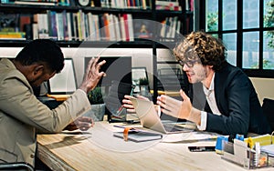 Two diverse Caucasian and African businessman seriously discussing with argument, disputing while sitting in modern meeting room