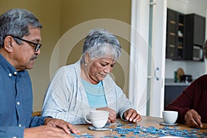 Two diverse female and male friends sitting at table and doing puzzles