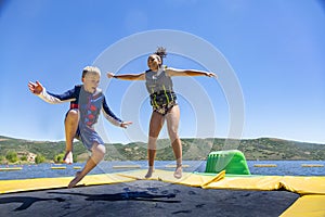 Two diverse kids jumping and playing on a water bounce house on a lake