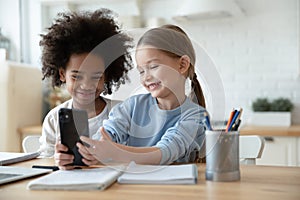 Two diverse little girls sisters having fun with smartphone together