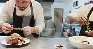 Two diverse male chefs decorating meals in kitchen, slow motion