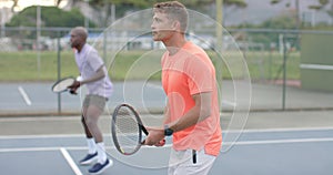 Two diverse male friends playing doubles returning ball on outdoor court in slow motion
