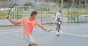 Two diverse male friends playing doubles returning ball on outdoor tennis court in slow motion